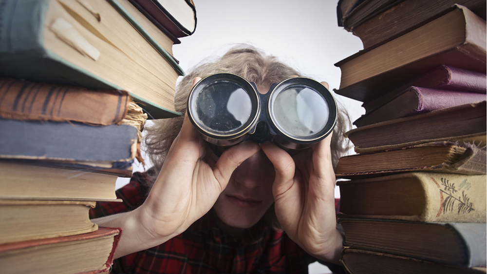 Stock image of someone between two stacks of books with binoculars